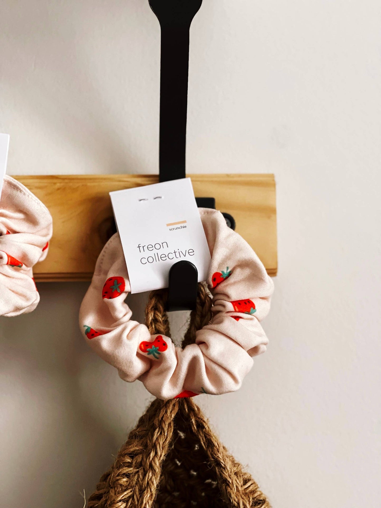 Freon Collective Organic Cotton Hair Scrunchie in Strawberry Pattern. Hanging on Black Hook with Basket.